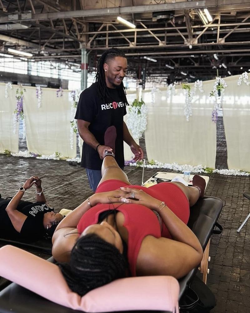 Owner Elijah Small smiling while stretching a client's leg at a pop-up event